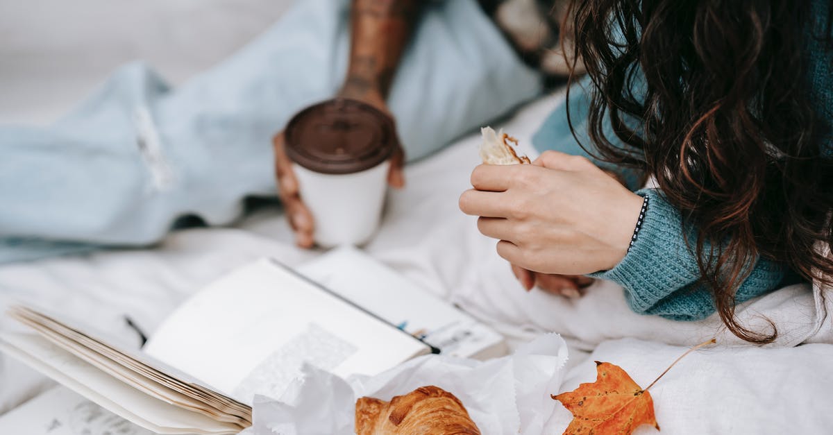 A book about croissants/viennoiserie - Unrecognizable multiracial couple with takeaway hot drink and croissant lying on white plaid with opened book during picnic in autumn day