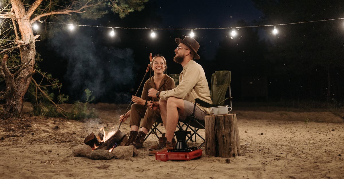 Adding 'netvet; to sausages - A Couple Sitting on Chair while Grilling on Campfire Adding 'netvet; to sausages - A Couple Sitting on Chair while Grilling on Campfire