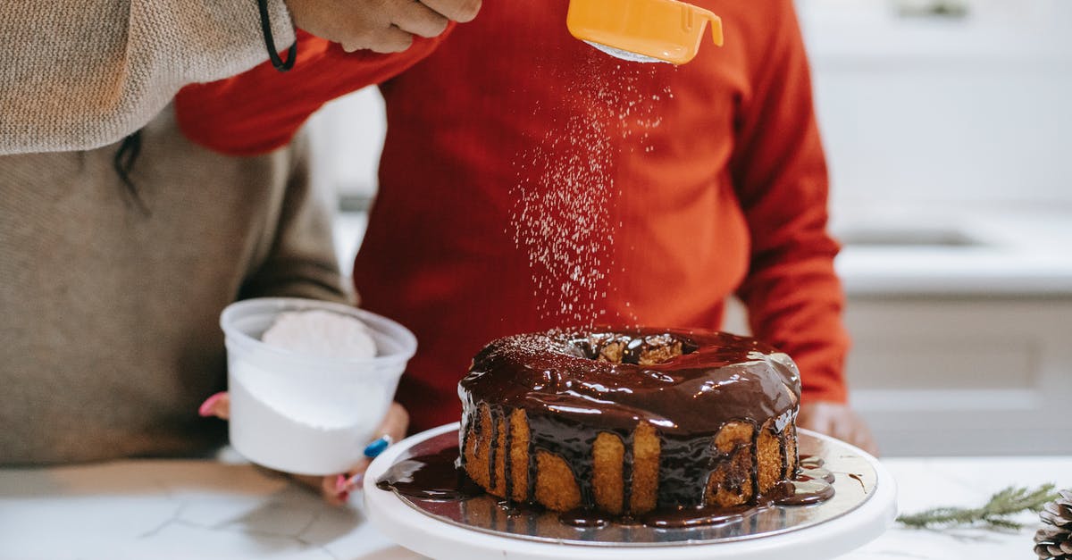 Adding melted chocolate to a sponge cake batter - Crop ethnic parent with child decorating cake with icing sugar Adding melted chocolate to a sponge cake batter - Crop ethnic parent with child decorating cake with icing sugar