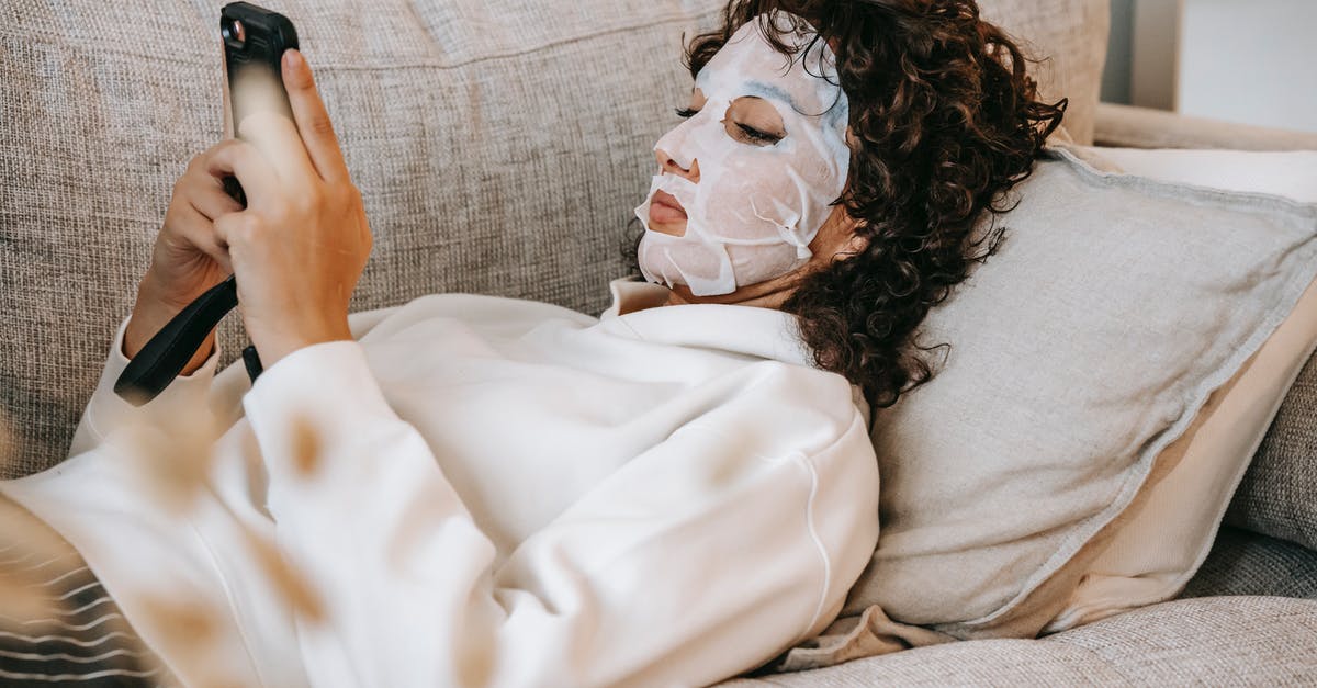 Adding moisture to gluten free muffins - Side view of female wearing facial moisturizing mask surfing cellphone while lying on couch in living room during skincare routine Adding moisture to gluten free muffins - Side view of female wearing facial moisturizing mask surfing cellphone while lying on couch in living room during skincare routine