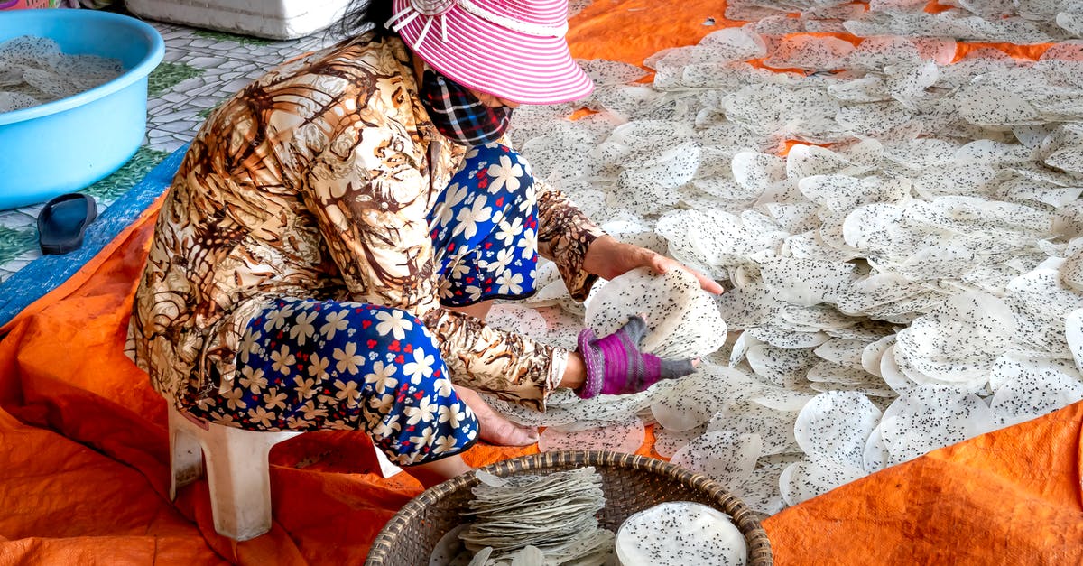Adding raw chia seeds to baked goods? - Side view of anonymous ethnic female in panama hat preparing rice sheets with chia seeds on textile Adding raw chia seeds to baked goods? - Side view of anonymous ethnic female in panama hat preparing rice sheets with chia seeds on textile