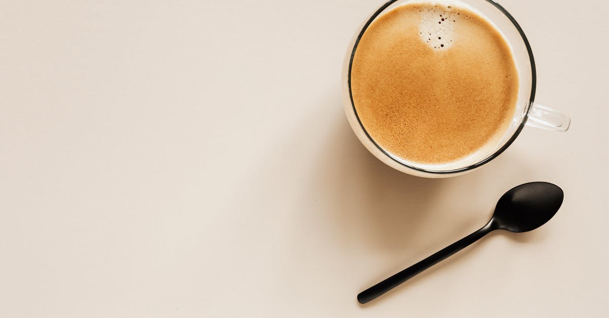 Air bubble on surface of chocolate - Top view of glass of aromatic light brown coffee with foam and small bubbles on top near metal spoon on beige surface Air bubble on surface of chocolate - Top view of glass of aromatic light brown coffee with foam and small bubbles on top near metal spoon on beige surface