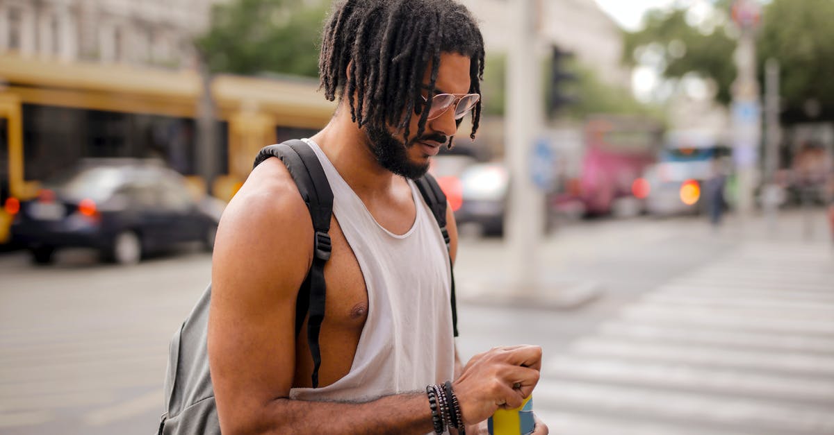 Am I missing something with Beer Can chicken? - Confident adult Hispanic male traveler in sunglasses and casual clothes with backpack opening can of drink while walking along pavement against blurred cars driving along street and empty crosswalk in downtown