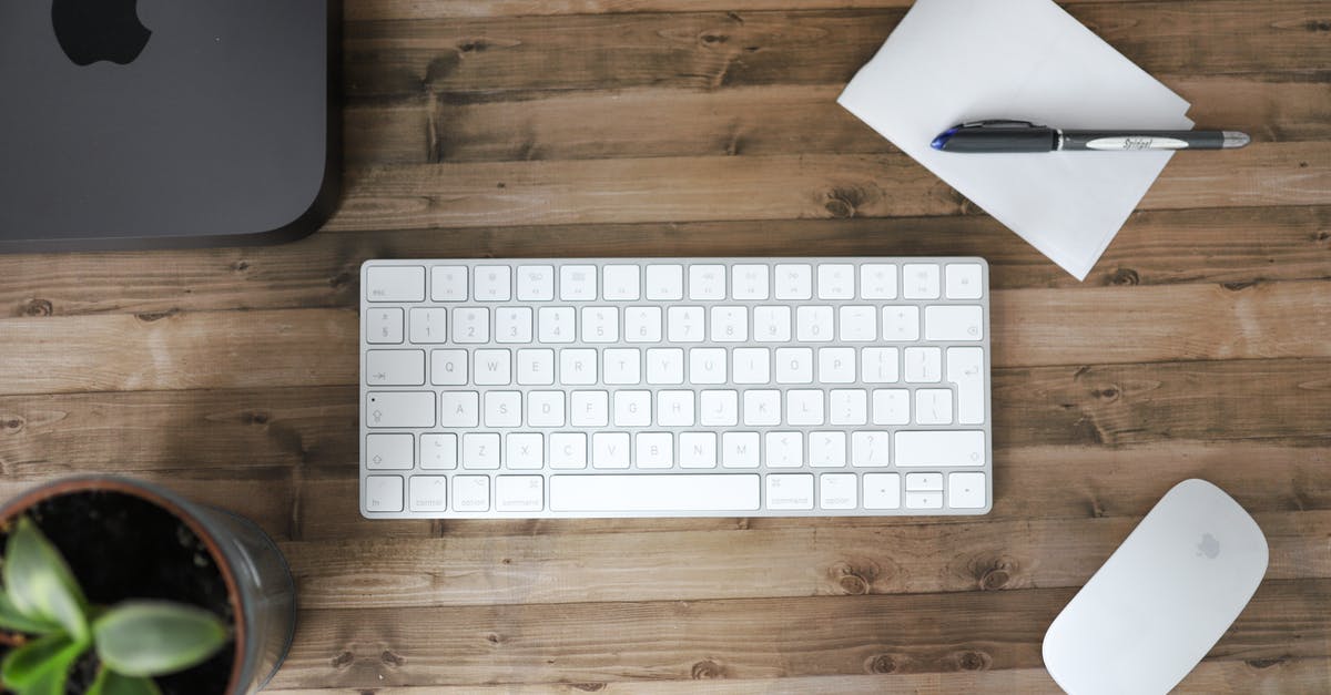 An electronic tool for mixing while the pot is on the fire - Overhead view of white keyboard and pen on paper for notes composing with black closed laptop and green pot plant on wooden table in bright workplace