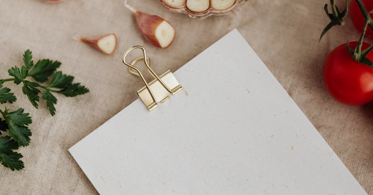 Are paper kitchen towels food-safe? - Top view of empty sheet of paper fixed with metal clip and placed near garlic gloves and ripe tomatoes with parsley on linen towel