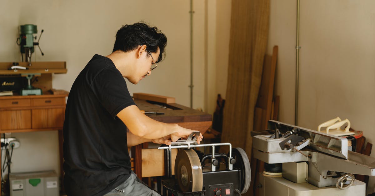 Are stone or metal grinding wheels better for flour? - Side view of young concentrated Asian male joiner working on grinder with sharp wheels while sitting on stool in workshop Are stone or metal grinding wheels better for flour? - Side view of young concentrated Asian male joiner working on grinder with sharp wheels while sitting on stool in workshop