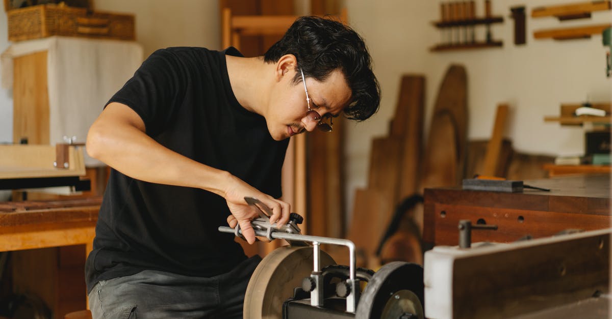 Are stone or metal grinding wheels better for flour? - Young attentive ethnic male joiner in eyewear sharpening manual instrument on grinder with wheels in light workroom Are stone or metal grinding wheels better for flour? - Young attentive ethnic male joiner in eyewear sharpening manual instrument on grinder with wheels in light workroom