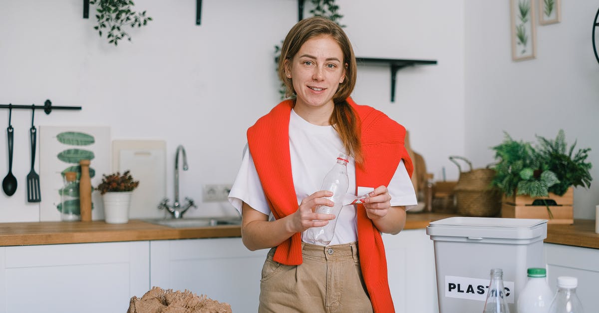 Bacteria contamination inside a thermos bottle - Female holding plastic bottle and looking at camera while sorting trash in blurred kitchen Bacteria contamination inside a thermos bottle - Female holding plastic bottle and looking at camera while sorting trash in blurred kitchen