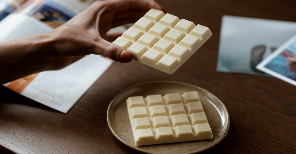 Bakers semi sweet chocolate bar - Crop faceless female holding piece of white chocolate while reading magazine and resting at home Bakers semi sweet chocolate bar - Crop faceless female holding piece of white chocolate while reading magazine and resting at home