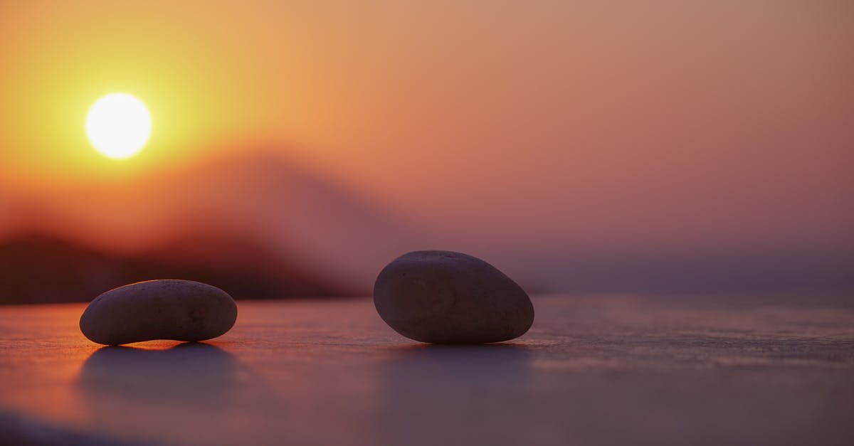 Baking below sea level - Ground level of stones on sandy shore near ocean behind mountains under bright sky with shining sun in twilight Baking below sea level - Ground level of stones on sandy shore near ocean behind mountains under bright sky with shining sun in twilight