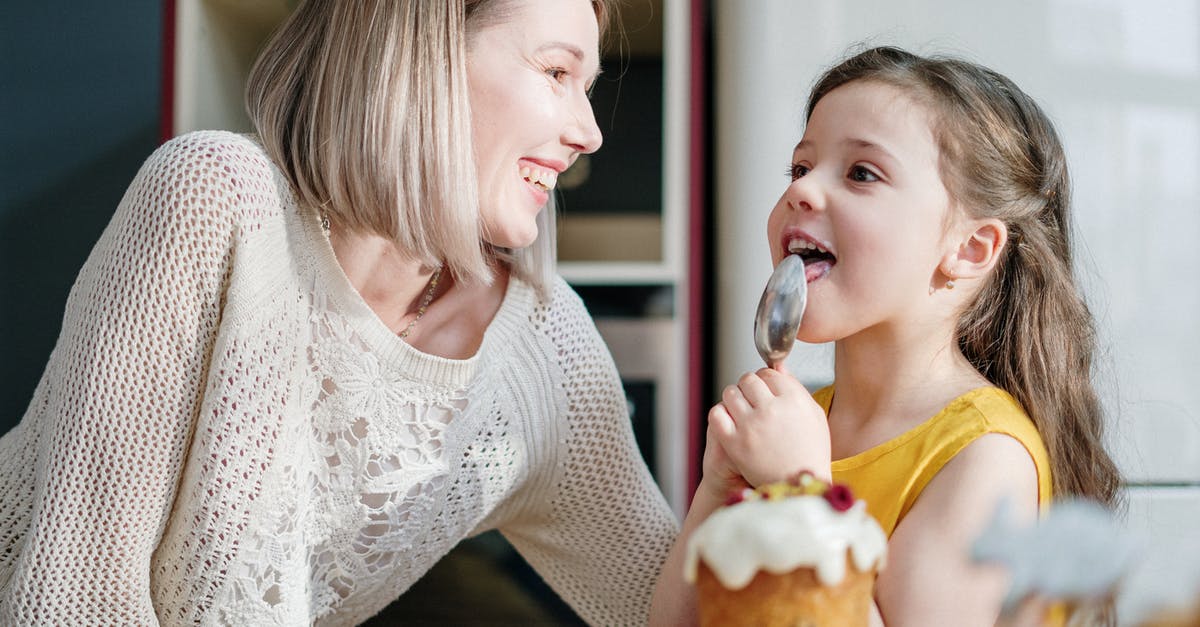 Baking Italian love cake - Woman in White Knit Sweater Smiling while Little Girl Licking Icing on Her Spoon Baking Italian love cake - Woman in White Knit Sweater Smiling while Little Girl Licking Icing on Her Spoon