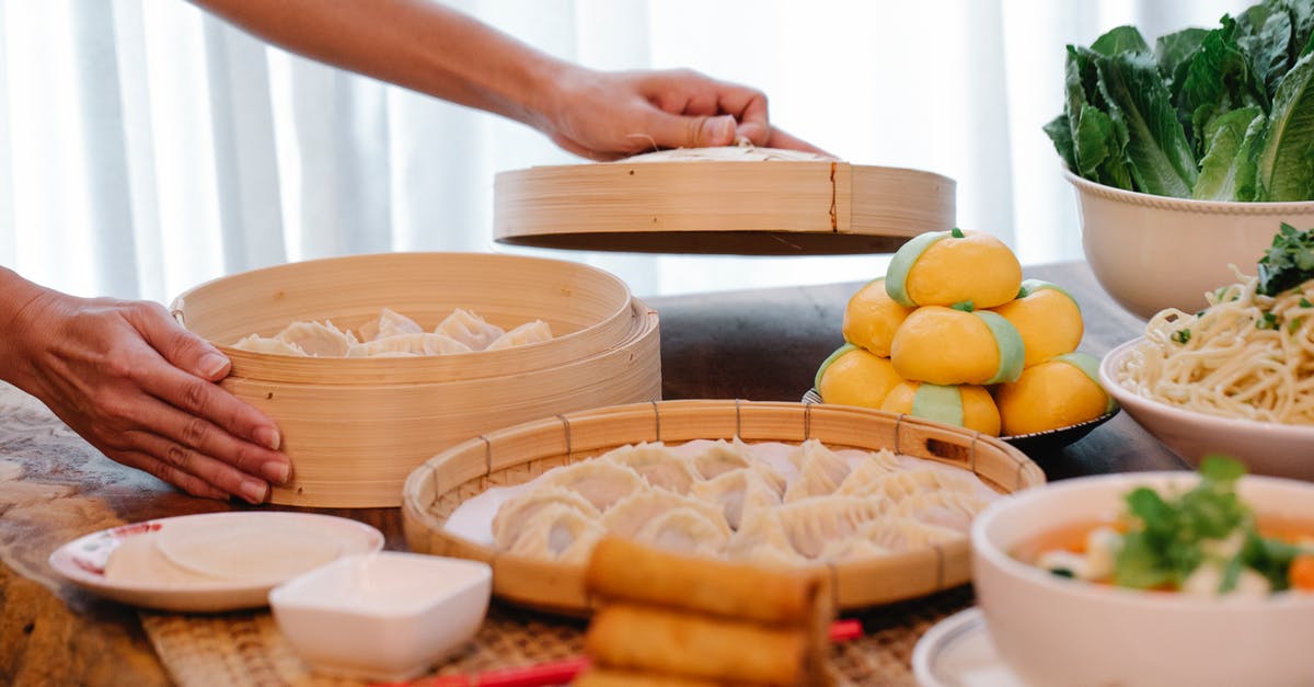 Bamboo Steamer VS Normal Steamer - Crop unrecognizable female standing at table with various Chinese dishes and uncooked jiaozi dumplings in bamboo steamer Bamboo Steamer VS Normal Steamer - Crop unrecognizable female standing at table with various Chinese dishes and uncooked jiaozi dumplings in bamboo steamer