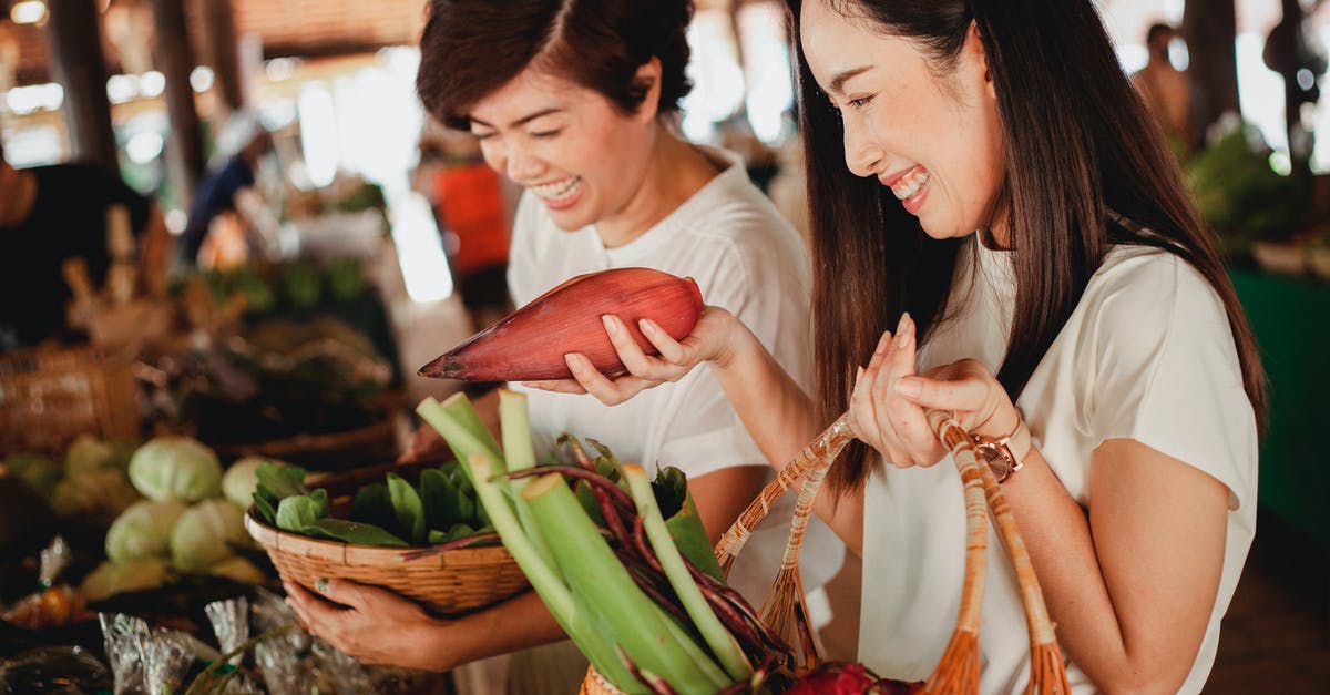 Banana blossoms versus bean sprouts - Crop Asian woman with banana flower near girlfriend in bazaar Banana blossoms versus bean sprouts - Crop Asian woman with banana flower near girlfriend in bazaar
