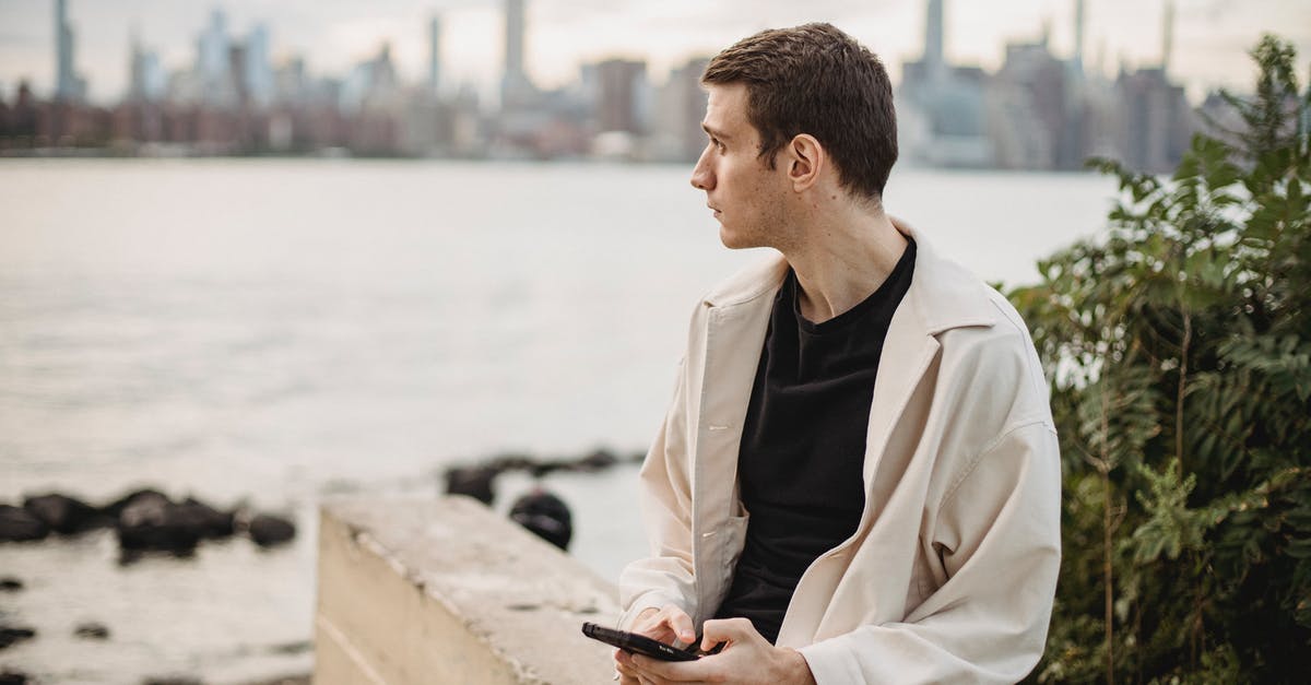 Bay used to crisp fermenting pickles - Pensive male messaging on mobile phone while sitting on border on waterfront near river and looking away Bay used to crisp fermenting pickles - Pensive male messaging on mobile phone while sitting on border on waterfront near river and looking away