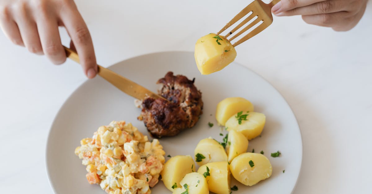 Beef parts interchangeability - From above of crop anonymous person with cutleries eating delicious fried cutlet and hot boiled potatoes with parsley garnished with nutritious Russian salad Beef parts interchangeability - From above of crop anonymous person with cutleries eating delicious fried cutlet and hot boiled potatoes with parsley garnished with nutritious Russian salad