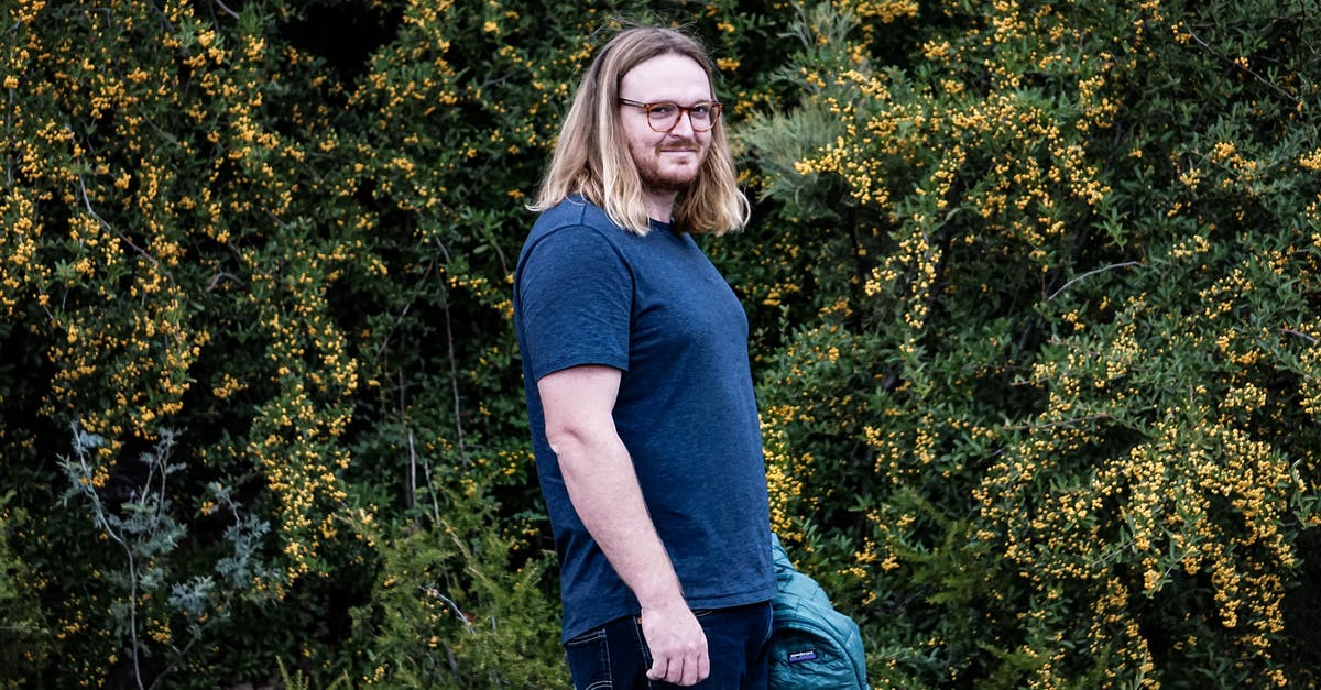berberis vulgaris vs berberis aristata - Side view of positive male with long hair in eyeglasses standing near barberry shrub berberis vulgaris vs berberis aristata - Side view of positive male with long hair in eyeglasses standing near barberry shrub