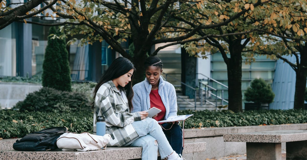 Best practices for using taps while avoiding cross contamination - Focused multiethnic students watching smartphone on city bench Best practices for using taps while avoiding cross contamination - Focused multiethnic students watching smartphone on city bench