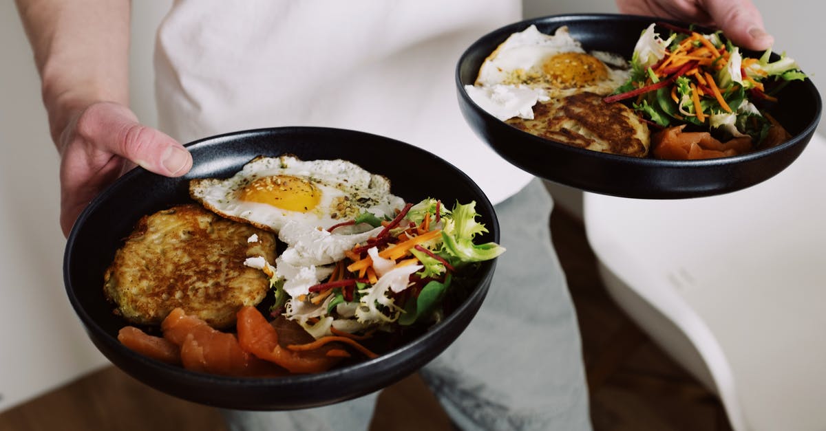 Best way to hold deep-fried foods? - Faceless male in white clothes holding black plates with fried eggs and fresh salad for breakfast in cozy kitchen