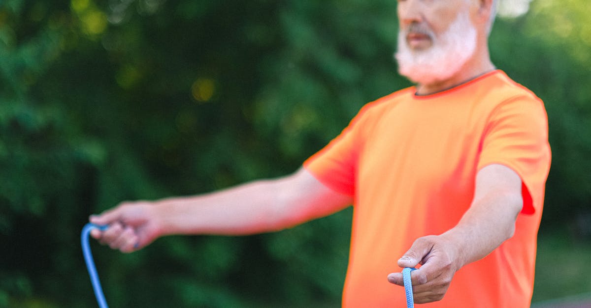 Bread crusty outside and super soft inside - Concentrated aged man in sportswear raising hands with skipping rope during workout on stadium in sunny day