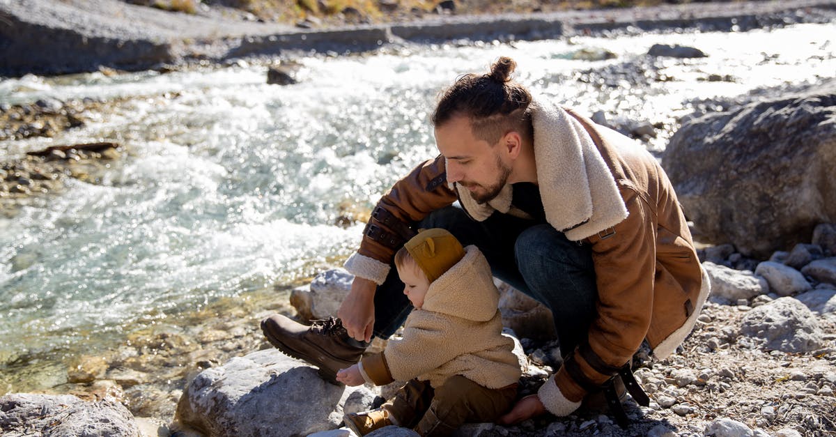 Bread Proving Time in Warm Climates - Bearded young father with little child in casual warm clothes sitting on rocky ground near river and enjoying time together while weekend Bread Proving Time in Warm Climates - Bearded young father with little child in casual warm clothes sitting on rocky ground near river and enjoying time together while weekend