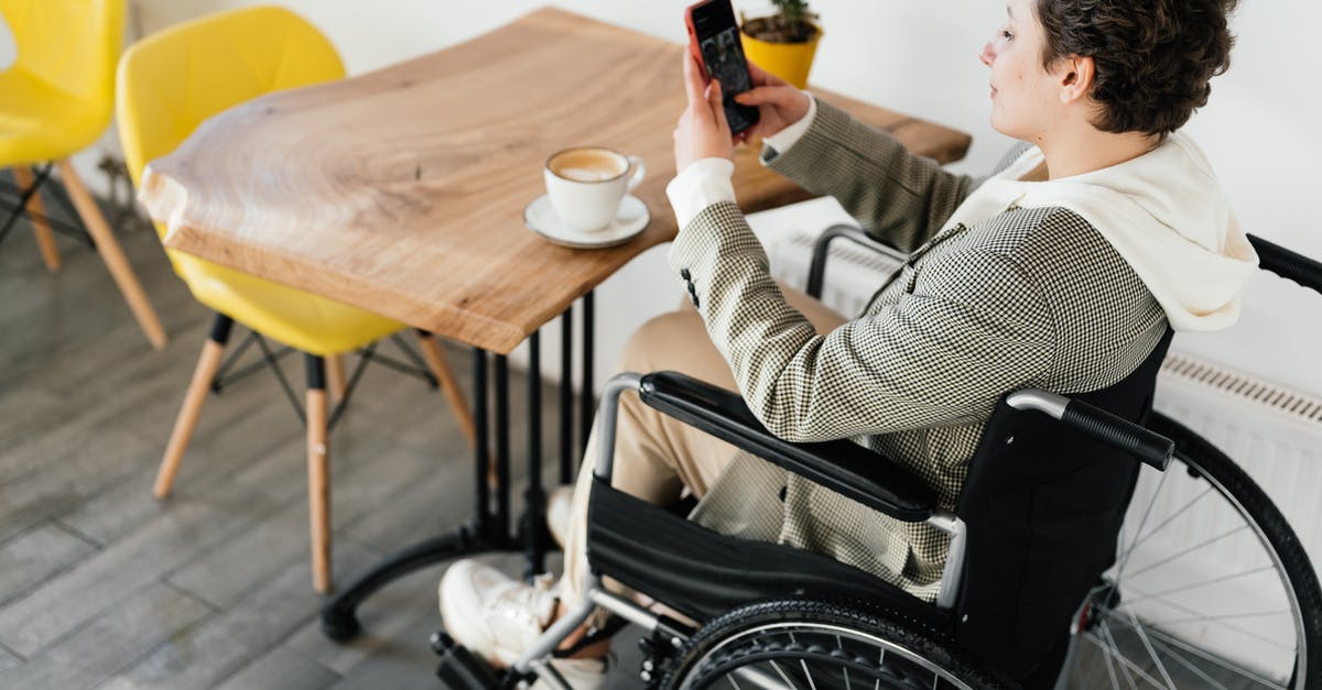 Brewing coffee concentrate using both hot and cold methods - Freezing concentrate - Side view full body of female in wheelchair taking picture of hot coffee while sitting at wooden table in cafeteria Brewing coffee concentrate using both hot and cold methods - Freezing concentrate - Side view full body of female in wheelchair taking picture of hot coffee while sitting at wooden table in cafeteria