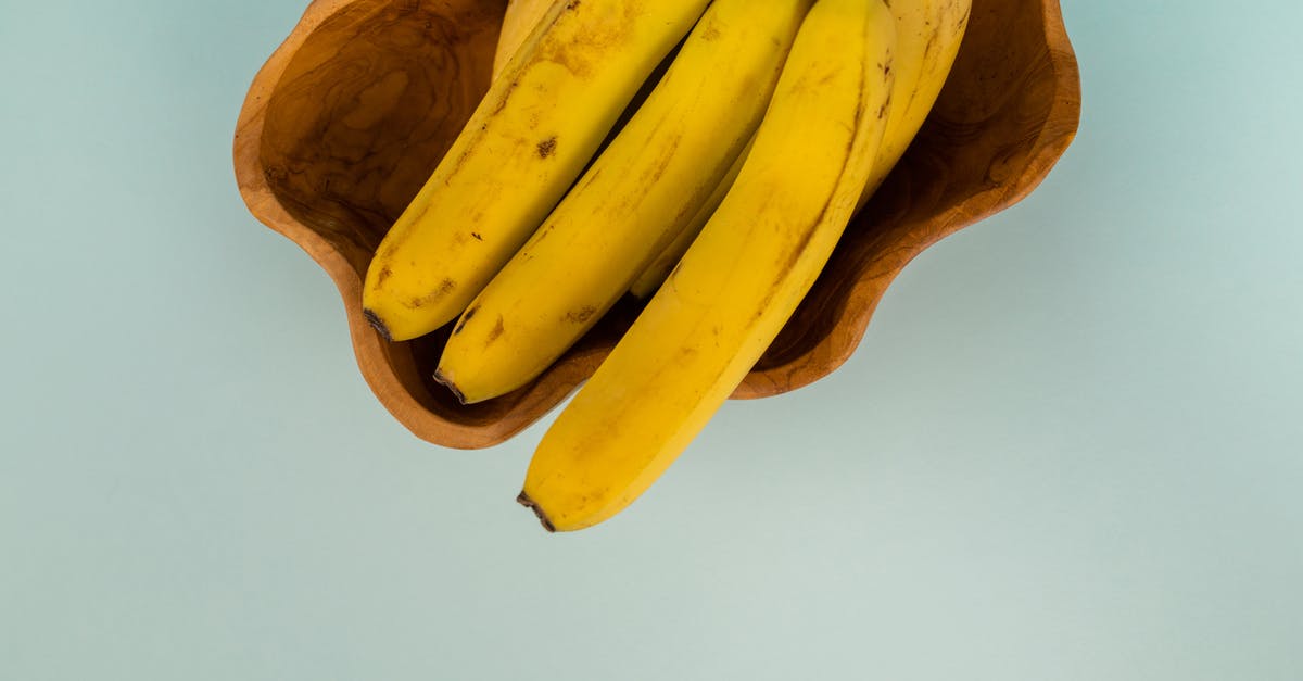 Brown spots in purple sweet potato - Top view of bunch of fresh bananas with blots on smooth yellow peel in curved bowl on light background