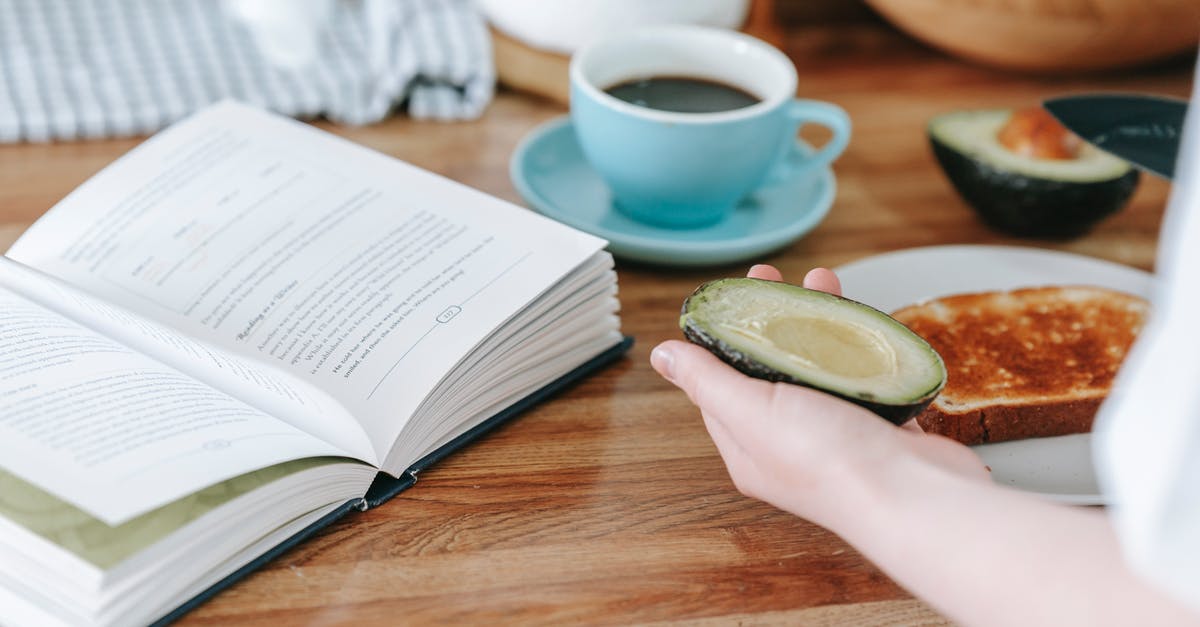 Calculating Nutrition Information for Commercial Food Labeling - Crop anonymous person sitting at table and reading book while having coffee and making toast with avocado for breakfast Calculating Nutrition Information for Commercial Food Labeling - Crop anonymous person sitting at table and reading book while having coffee and making toast with avocado for breakfast