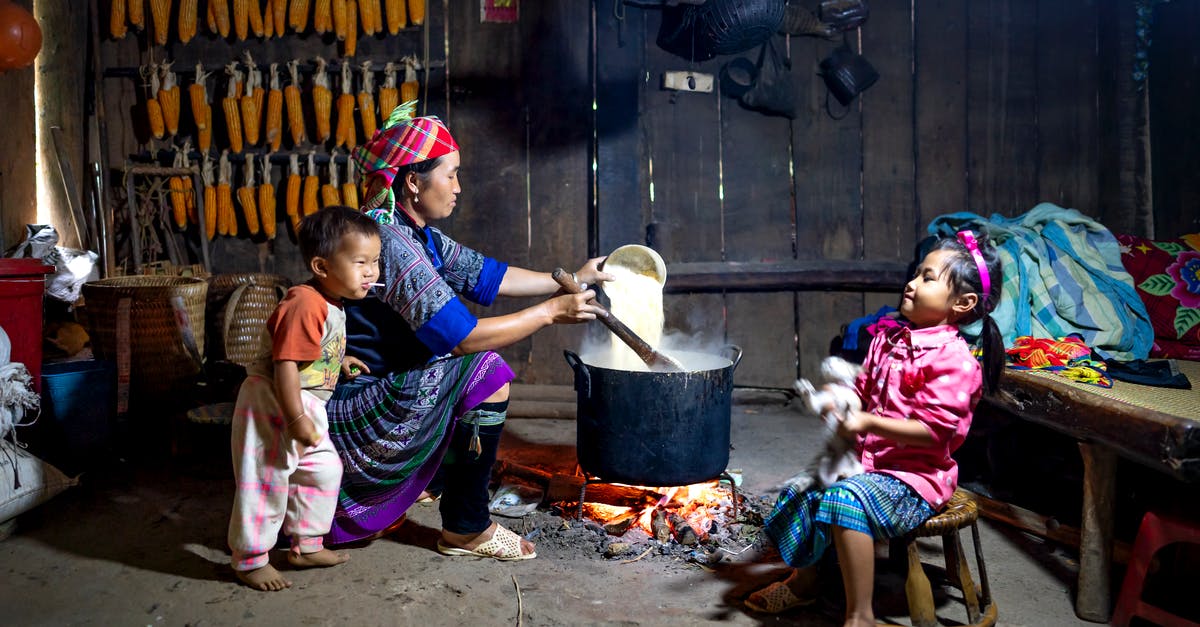 Can a Toddler Eat Food Cooked With Honey in it? - Ethnic mother pouring rice into pot on fire against daughter with cat and barefoot baby eating lollipop at home Can a Toddler Eat Food Cooked With Honey in it? - Ethnic mother pouring rice into pot on fire against daughter with cat and barefoot baby eating lollipop at home