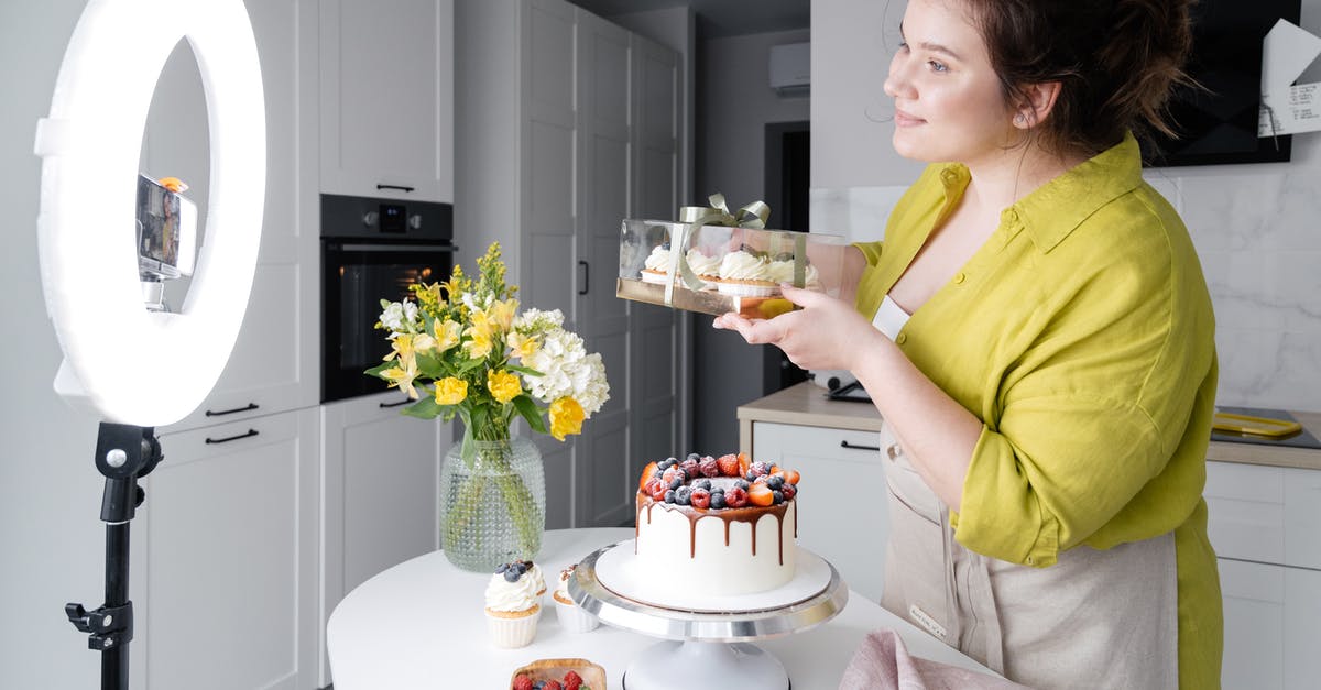 Can I broil a box cake in the oven? - Side view of positive young female food blogger in casual clothes and apron introducing yummy cakes and smiling while standing in front of ring lamp and recording vlog on smartphone Can I broil a box cake in the oven? - Side view of positive young female food blogger in casual clothes and apron introducing yummy cakes and smiling while standing in front of ring lamp and recording vlog on smartphone