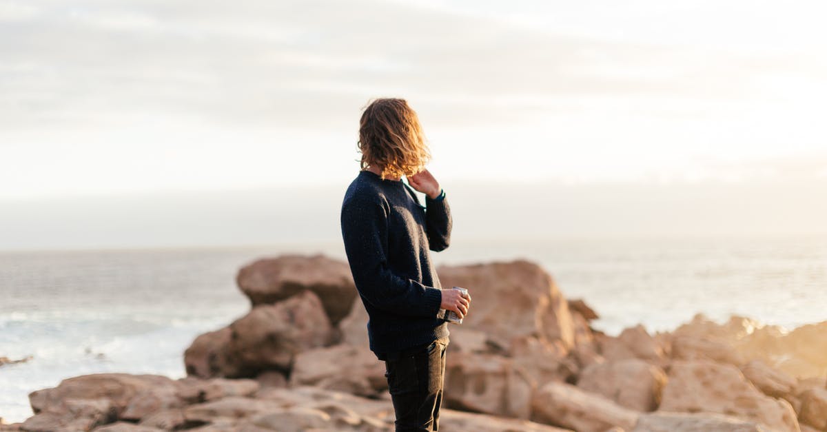 Can I dissolve mint in water and drink it? - Side view of anonymous male traveler with can of beverage admiring ocean from rough rocks under shiny sky in evening