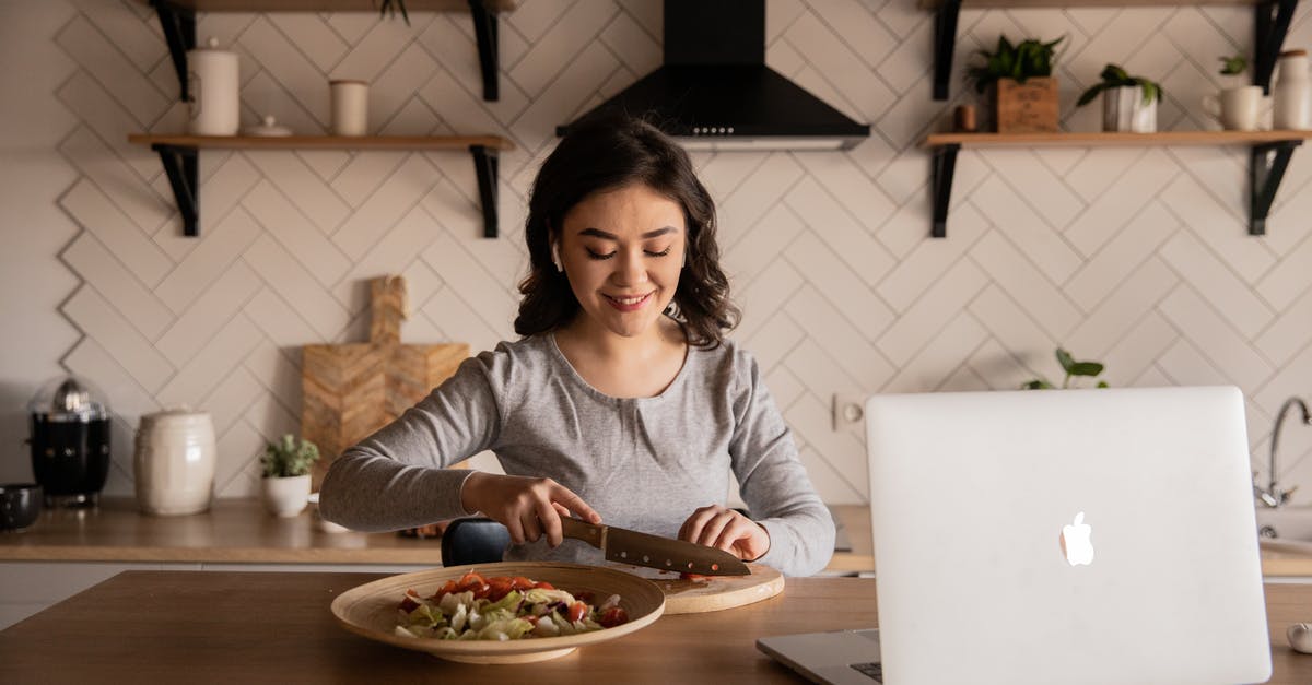 Can you hone a knife properly by using another knife? - Cheerful ethnic female cutting fresh vegetables on cutting board while sitting at wooden table in kitchen with open portable computer in apartment Can you hone a knife properly by using another knife? - Cheerful ethnic female cutting fresh vegetables on cutting board while sitting at wooden table in kitchen with open portable computer in apartment