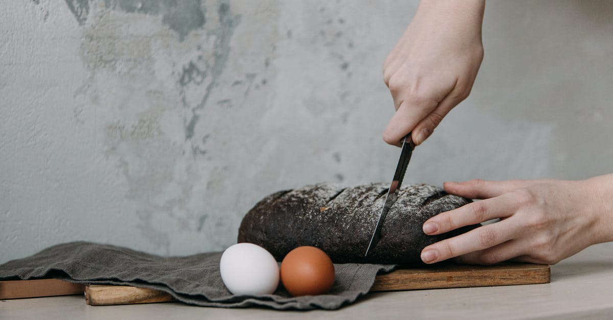 Cast Iron Bread Tin is Leaving Black Spots on Bread? - Photo of a Person's Hands Slicing a Black Loaf of Bread Cast Iron Bread Tin is Leaving Black Spots on Bread? - Photo of a Person's Hands Slicing a Black Loaf of Bread