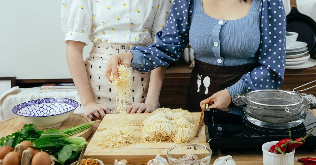 Chinese noodle dough breaking when pulled - Crop anonymous ladies in aprons standing near wooden table with various ingredients and utensil while preparing to cook homemade pasta together Chinese noodle dough breaking when pulled - Crop anonymous ladies in aprons standing near wooden table with various ingredients and utensil while preparing to cook homemade pasta together