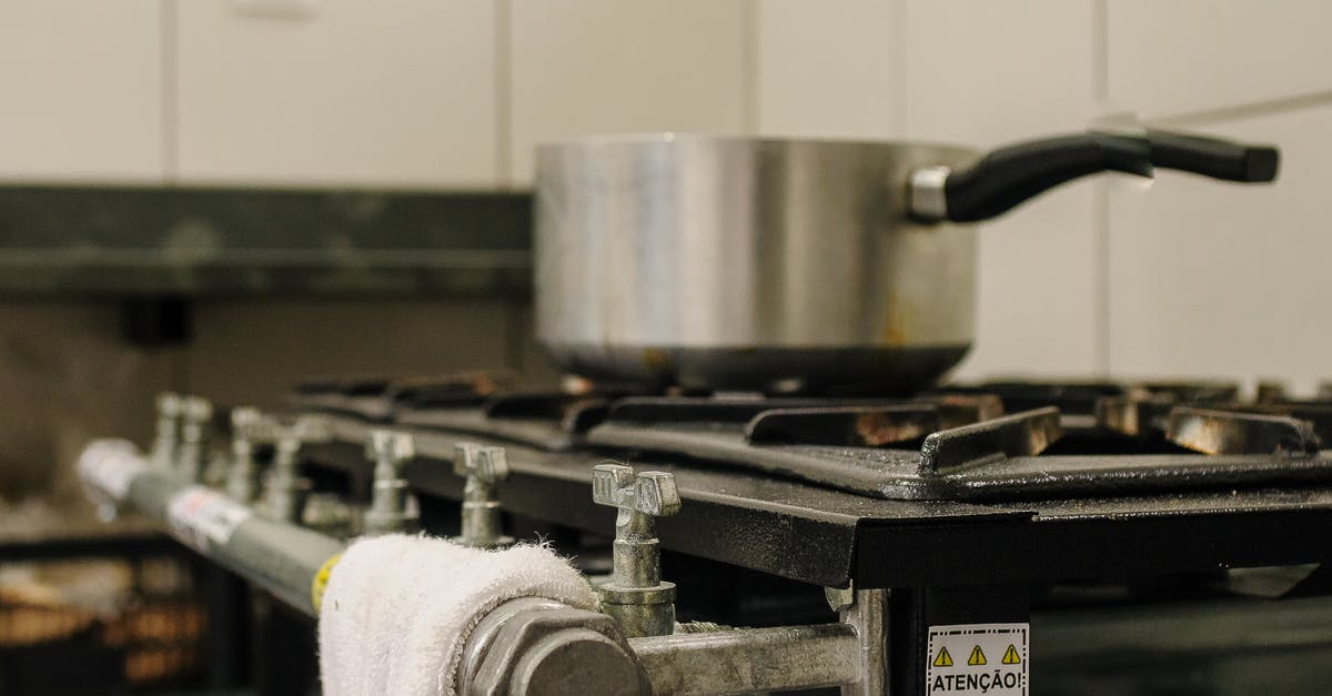 choosing a saucepan material for creams and caramels - Saucepan on rack of old gas stove with valves in row and sticker with attention symbol against fabric choosing a saucepan material for creams and caramels - Saucepan on rack of old gas stove with valves in row and sticker with attention symbol against fabric