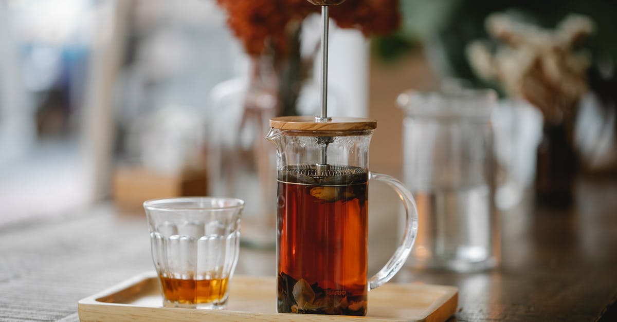 Cleaning a tea pot - Transparent French press with hot aromatic herbal tea brewing on wooden tray near glass on table in cafe Cleaning a tea pot - Transparent French press with hot aromatic herbal tea brewing on wooden tray near glass on table in cafe
