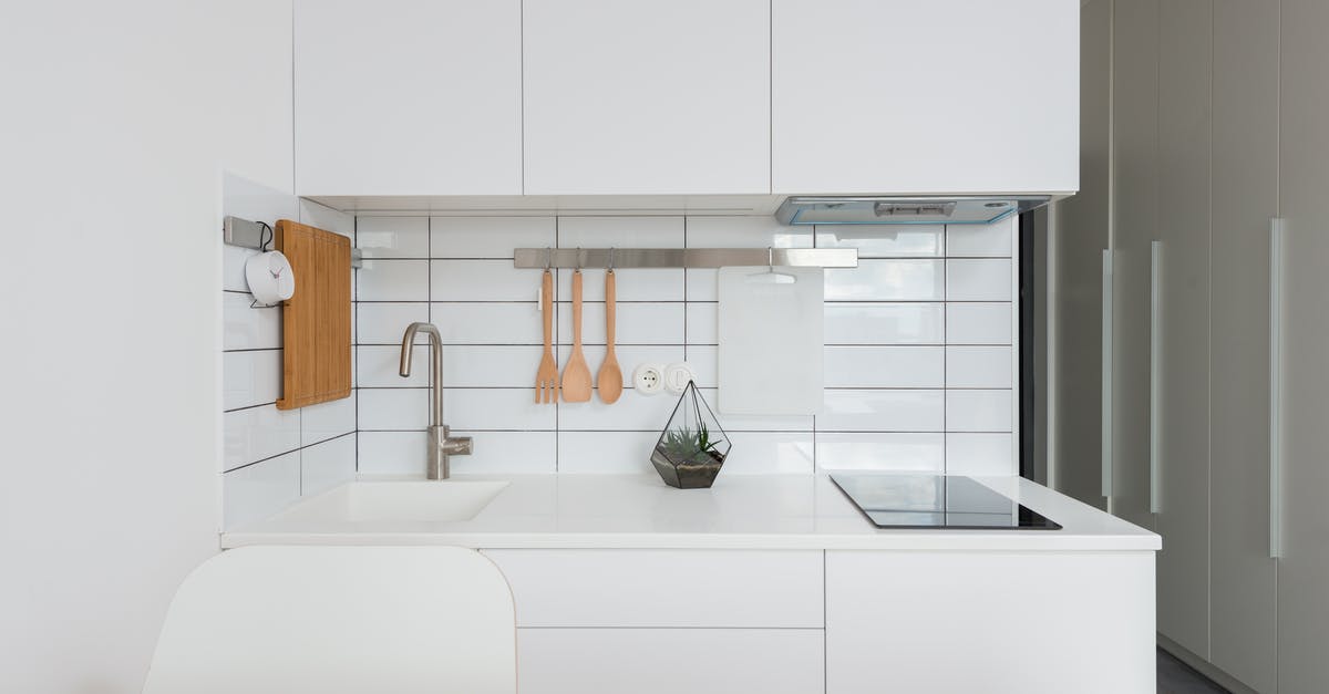 Cleaning white bubbles on induction stove - Wooden table placed near white cupboards in modern kitchen with minimalist interior in daylight Cleaning white bubbles on induction stove - Wooden table placed near white cupboards in modern kitchen with minimalist interior in daylight