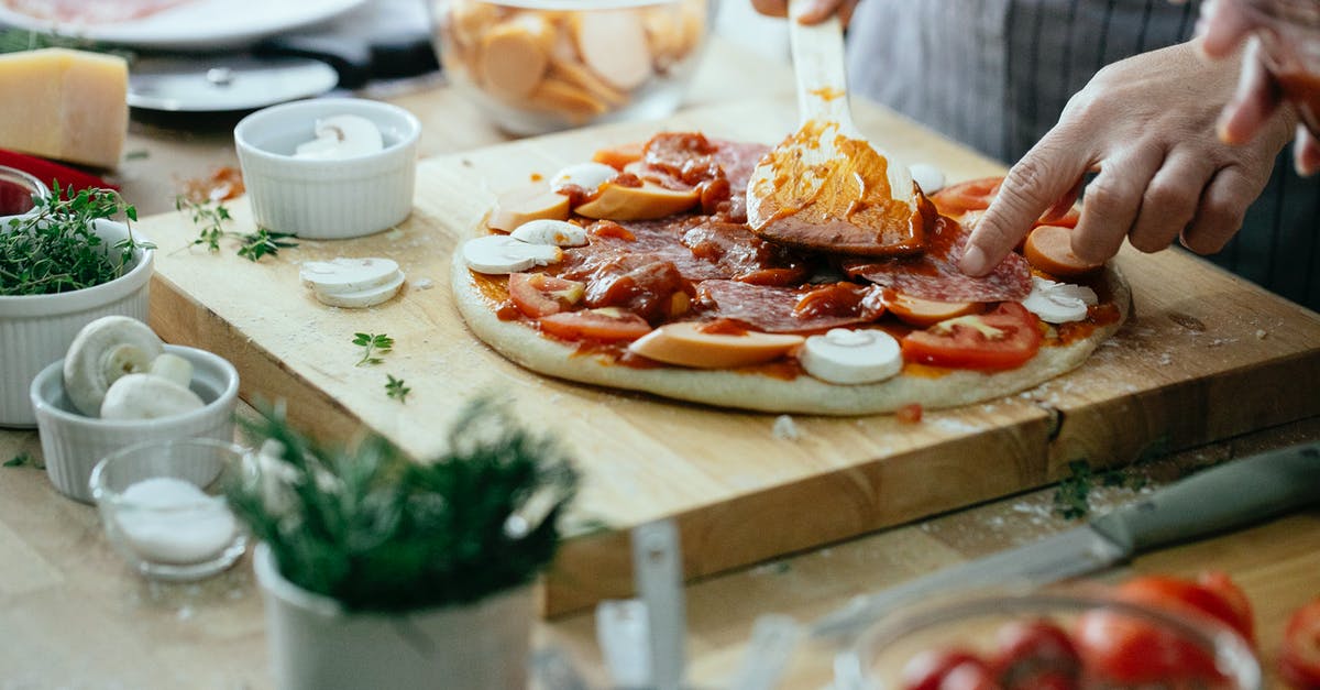Cooked or raw mushrooms on pizza? - Unrecognizable chef spreading sauce on pizza with tomatoes mushrooms and salami placed on wooden cutting board on table with ingredients Cooked or raw mushrooms on pizza? - Unrecognizable chef spreading sauce on pizza with tomatoes mushrooms and salami placed on wooden cutting board on table with ingredients