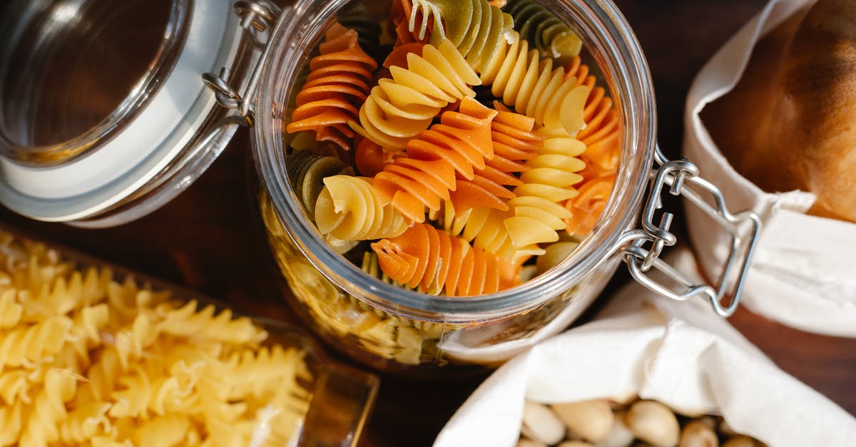 Cracking open a pistachio - From above glass jar with colorful rotini placed on table near fusilli in container and pistachios and bread in bags Cracking open a pistachio - From above glass jar with colorful rotini placed on table near fusilli in container and pistachios and bread in bags