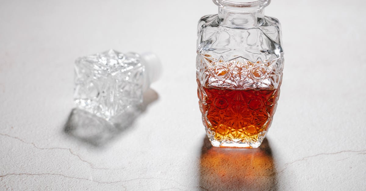 Cracking open a pistachio - From above of open crystal glass jug with alcoholic beverage placed on white table with cracks Cracking open a pistachio - From above of open crystal glass jug with alcoholic beverage placed on white table with cracks