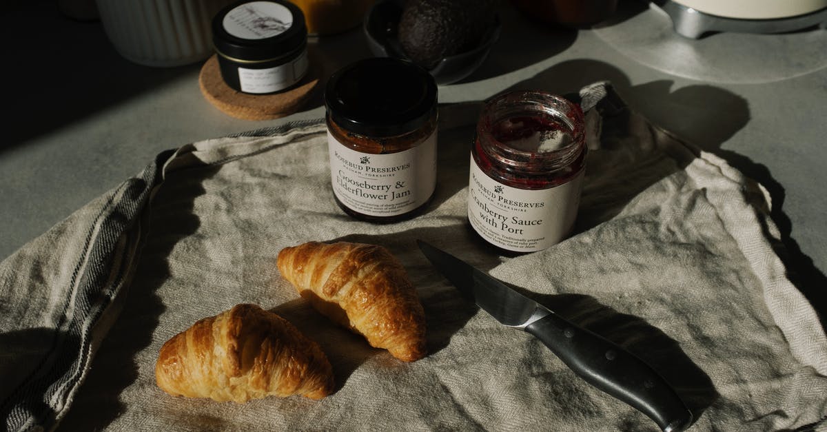 Crusty french bread - Still life of delicious brown croissants with opened jam and sauce pots on gray kitchen counter placed on with fabric napkin near knife in rustic style Crusty french bread - Still life of delicious brown croissants with opened jam and sauce pots on gray kitchen counter placed on with fabric napkin near knife in rustic style