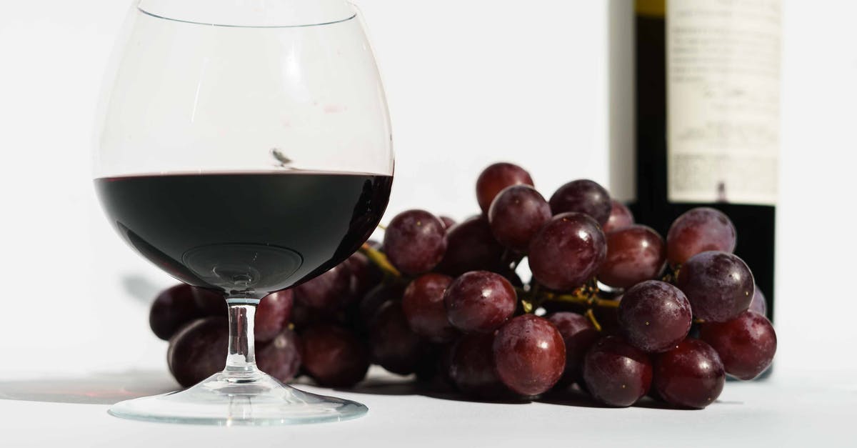 Crystals on bottle of sweet alcohol - Glass of red fragrant wine placed near bunch of sweet grapes and bottle in white studio Crystals on bottle of sweet alcohol - Glass of red fragrant wine placed near bunch of sweet grapes and bottle in white studio