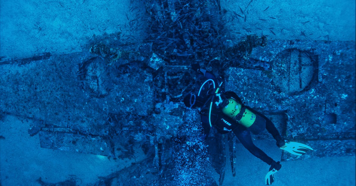 Damage to pan bottom - Top view of unrecognizable person in wetsuit inspecting rough remains of sunken plane on bottom of sea Damage to pan bottom - Top view of unrecognizable person in wetsuit inspecting rough remains of sunken plane on bottom of sea