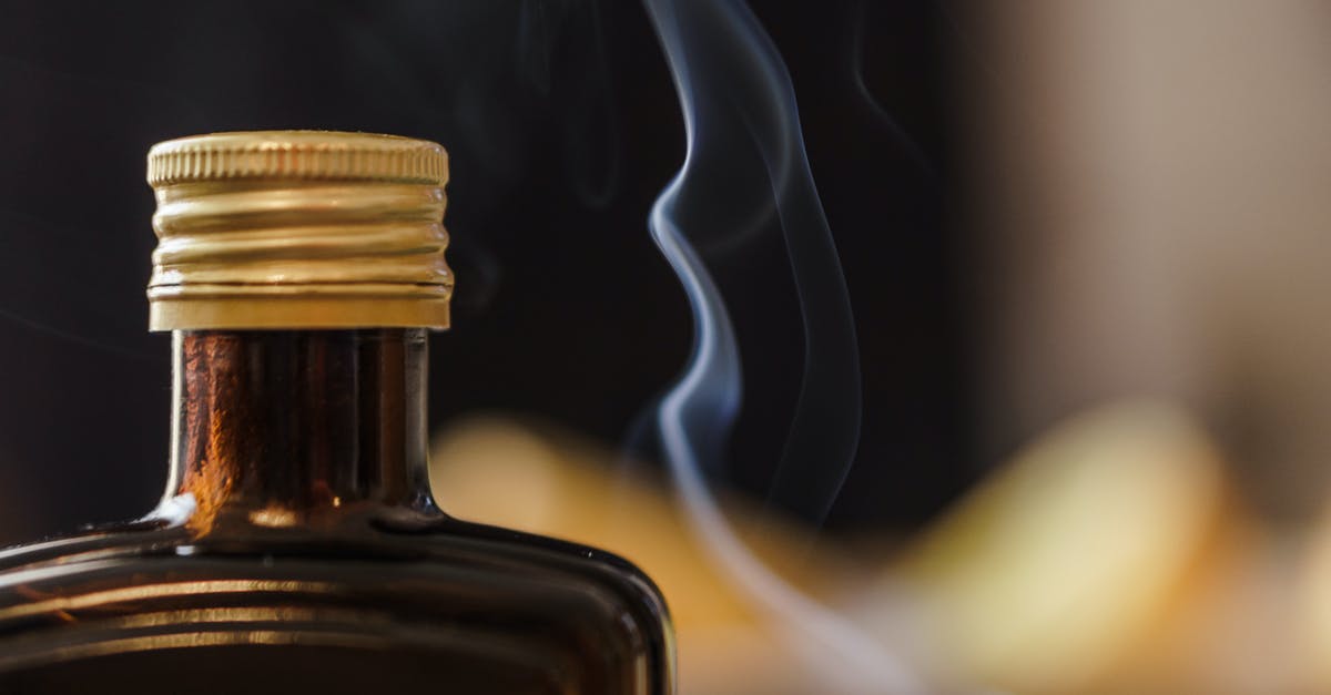 Date cookies are thin and spread out - Shiny bottle of alcohol with opaque glass and ribbed cap near fume in air on blurred background Date cookies are thin and spread out - Shiny bottle of alcohol with opaque glass and ribbed cap near fume in air on blurred background