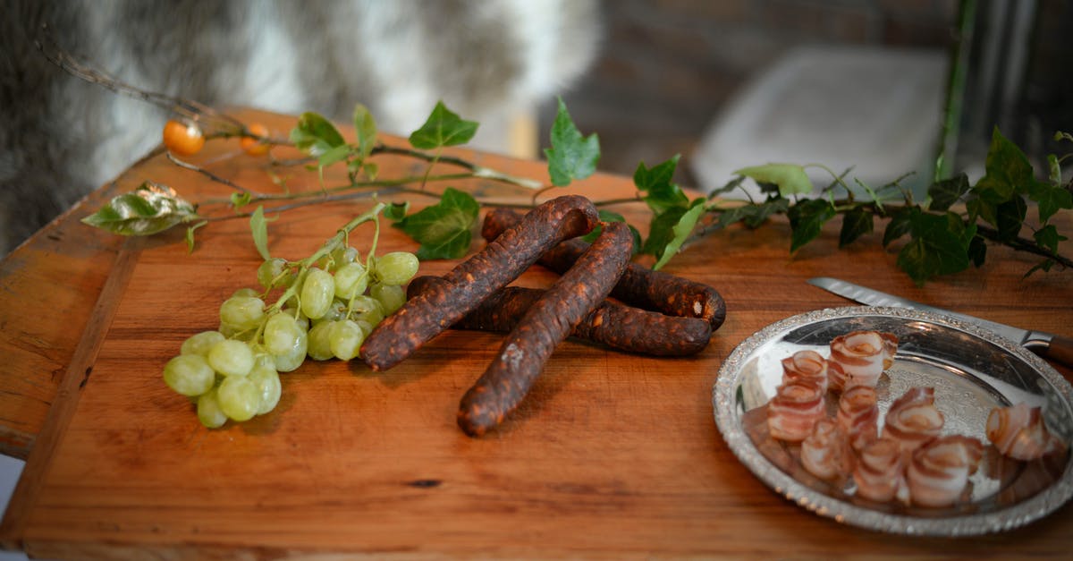 Dealing with a hank of natural sausage casings - From above of appetizing sausages placed near branch of grapes and bacon plate on wooden board Dealing with a hank of natural sausage casings - From above of appetizing sausages placed near branch of grapes and bacon plate on wooden board