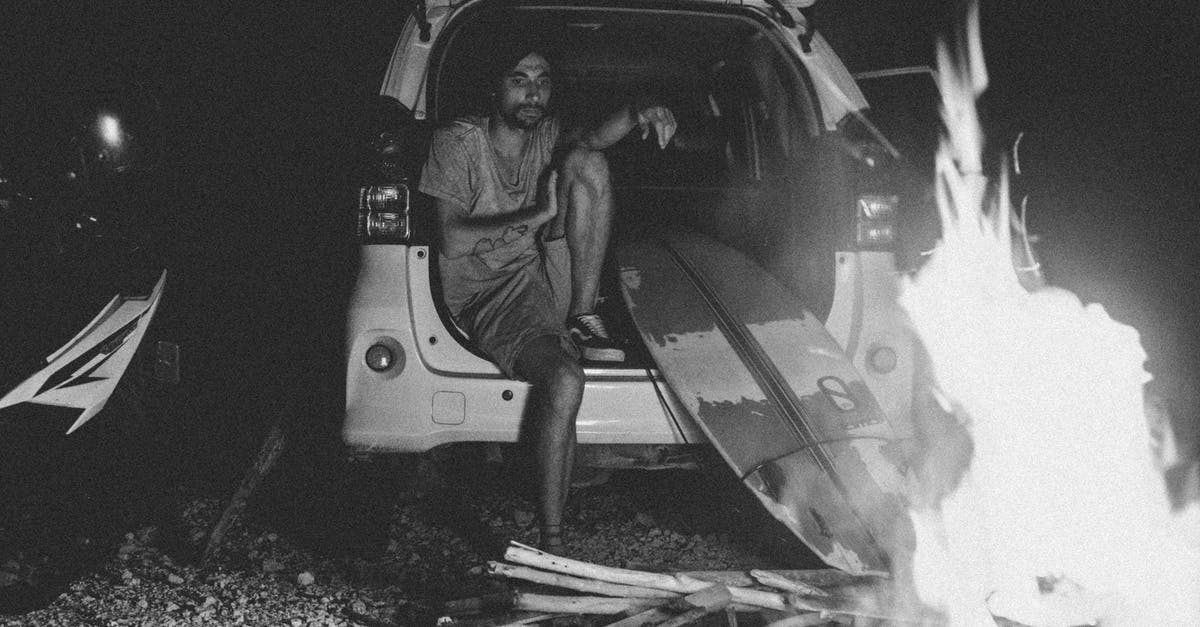 deli ham left in warm car - Black and white bearded young male surfer in summer clothes recreating in SUV car trunk and looking at bonfire at night deli ham left in warm car - Black and white bearded young male surfer in summer clothes recreating in SUV car trunk and looking at bonfire at night