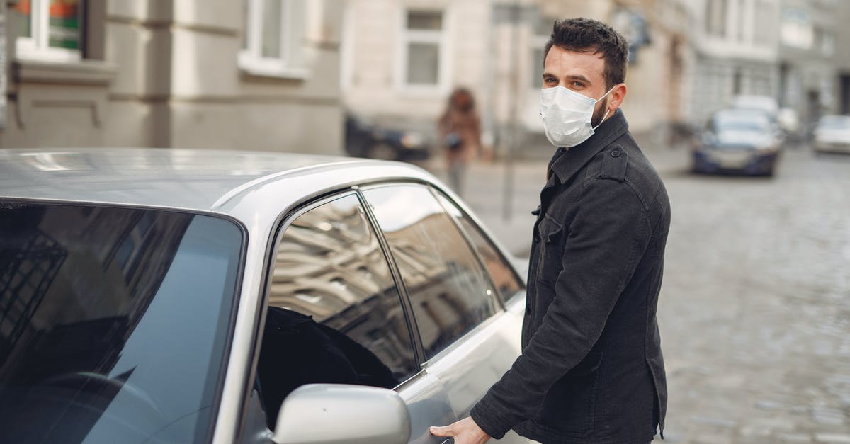 deli ham left in warm car - Bearded male driver wearing warm jacket and protective facial mask opening door of auto on blurred city background during Coronavirus pandemic and looking at camera deli ham left in warm car - Bearded male driver wearing warm jacket and protective facial mask opening door of auto on blurred city background during Coronavirus pandemic and looking at camera