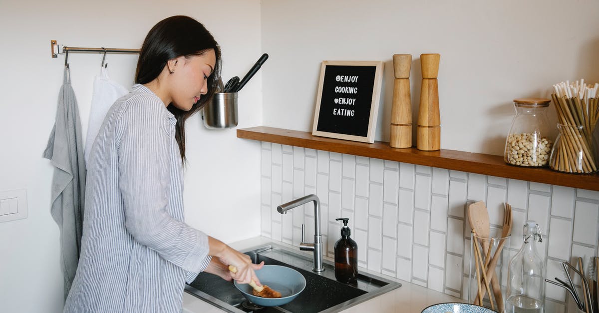 Detergent Contamination of Processed Foods - Side view of Asian female with brush washing dishes at sink while doing housework in light kitchen with supplies at home Detergent Contamination of Processed Foods - Side view of Asian female with brush washing dishes at sink while doing housework in light kitchen with supplies at home