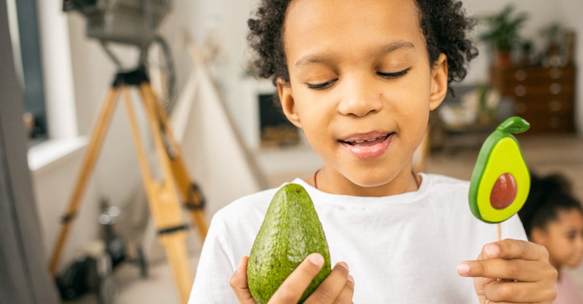 Determining sugar content of liqueurs - Cute black boy with lollipop and avocado in hands Determining sugar content of liqueurs - Cute black boy with lollipop and avocado in hands