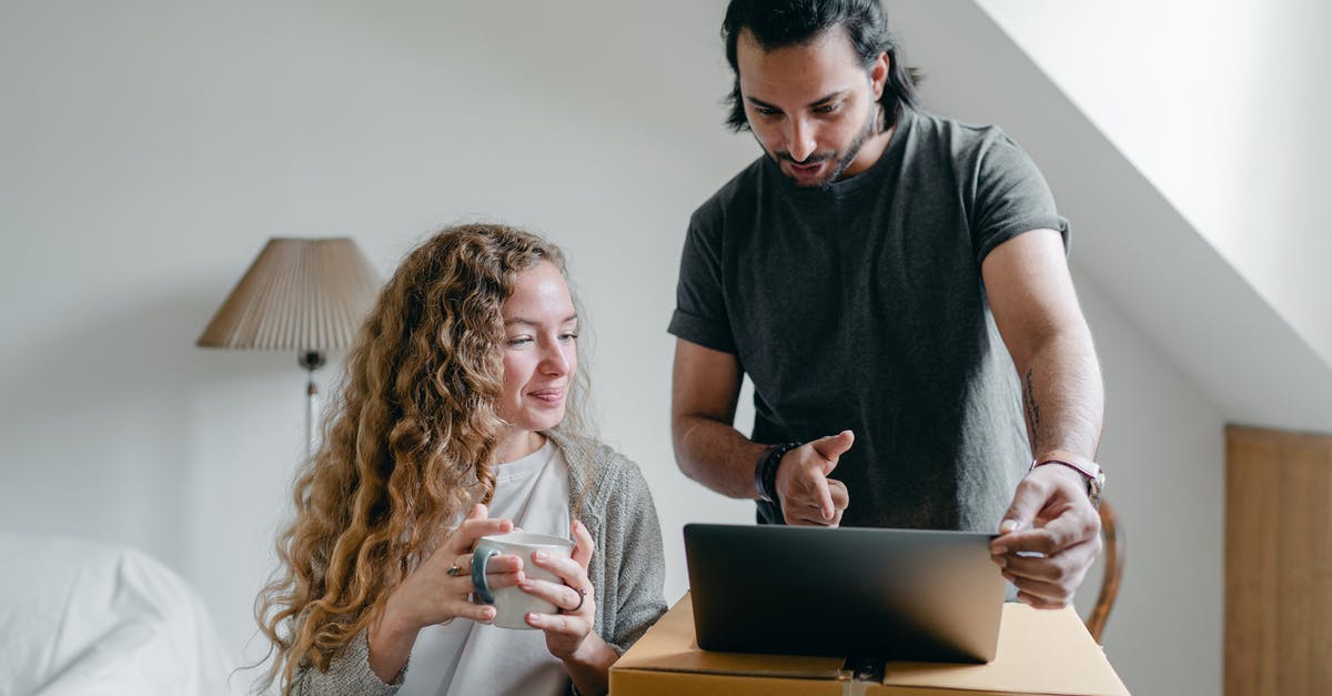 Device to squeeze last yogurt out of carton - Positive happy young couple in casual clothes packing belongings into carton box and using laptop in living room near window Device to squeeze last yogurt out of carton - Positive happy young couple in casual clothes packing belongings into carton box and using laptop in living room near window