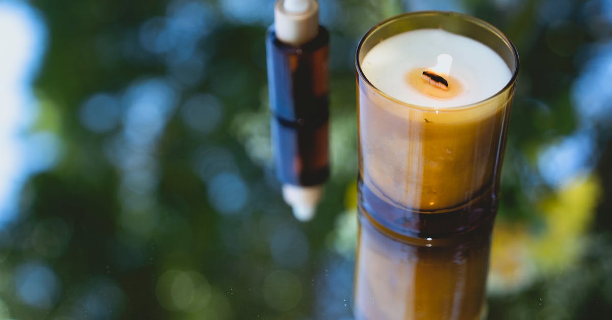 Did I just almost start an oil fire? - High angle of fragrant burning candle placed near amber glass bottle of essential oil on reflecting table Did I just almost start an oil fire? - High angle of fragrant burning candle placed near amber glass bottle of essential oil on reflecting table